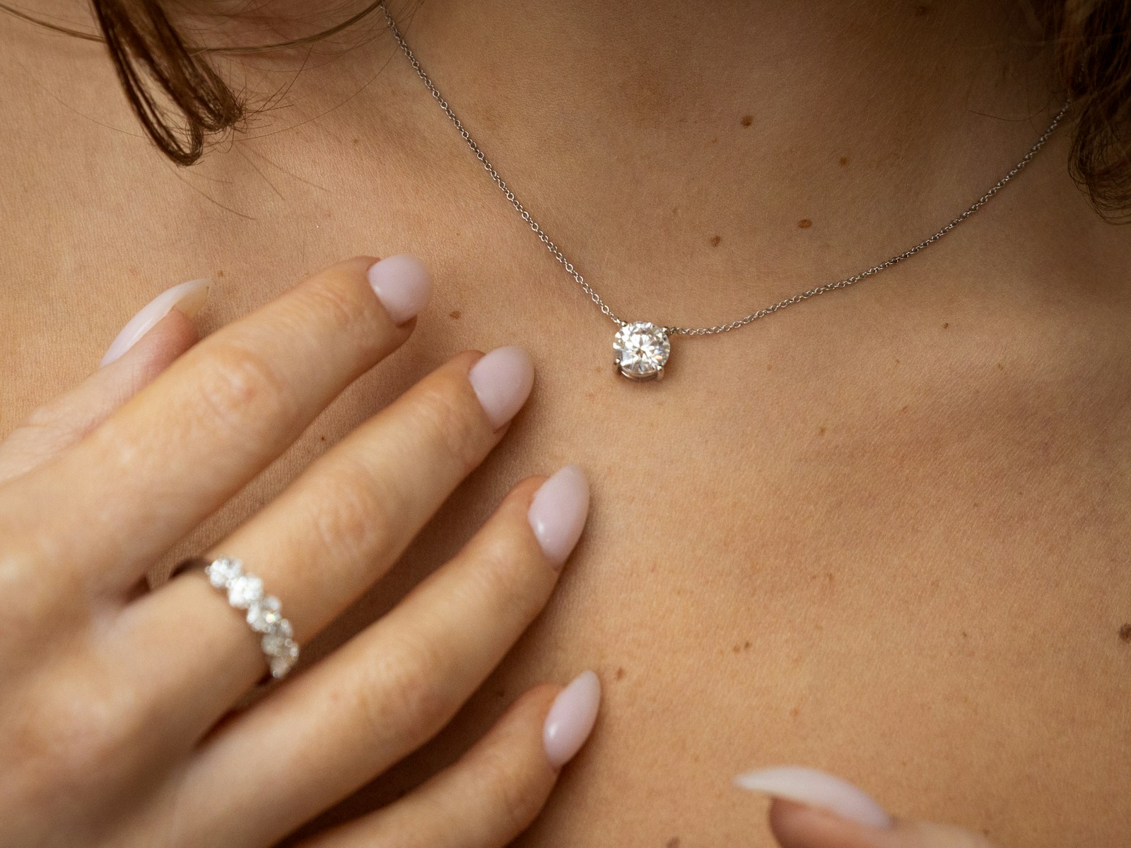 A diamond pendant and ring against warm skin
