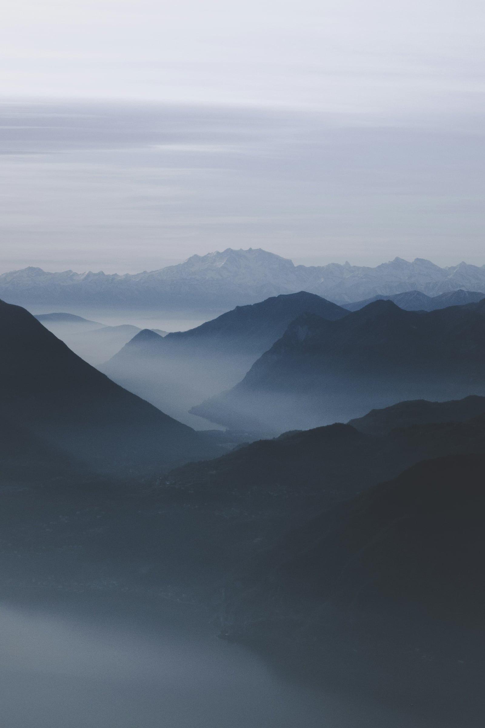 Layers of blue mountain ridges recede into mist beneath a pale overcast sky.