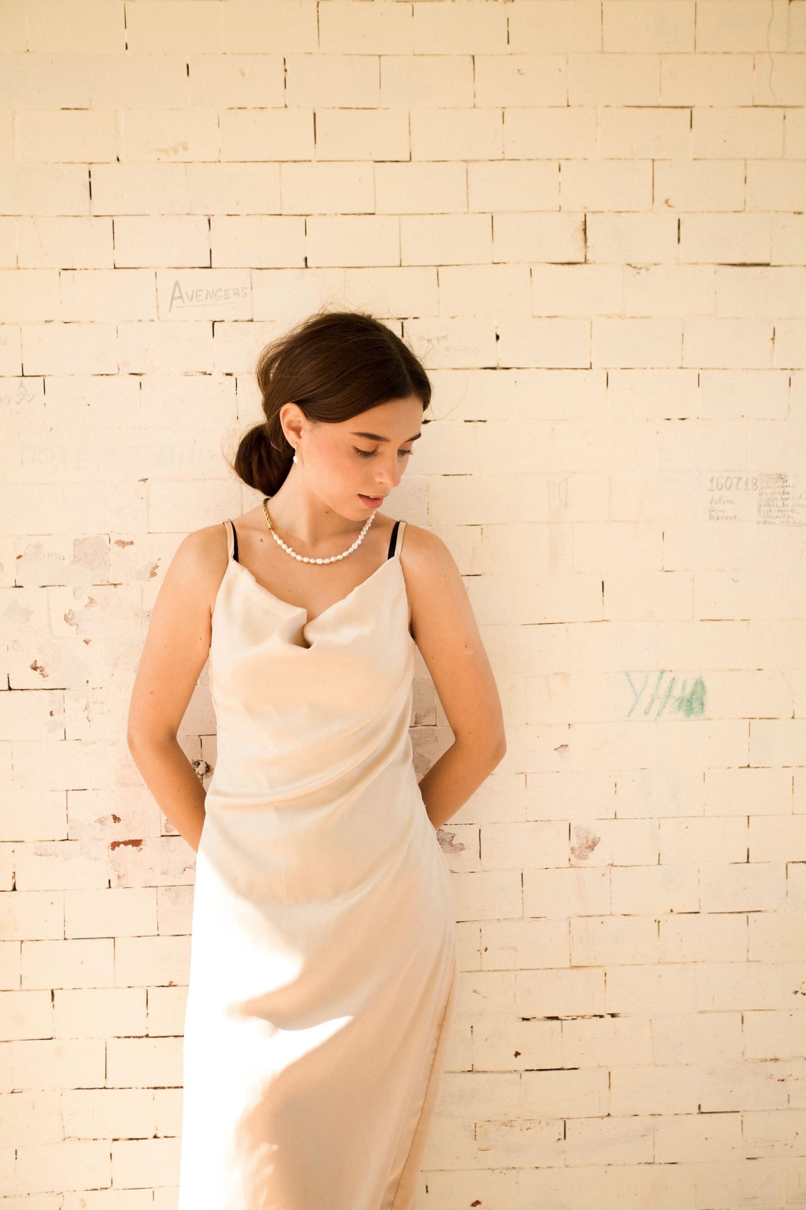 A woman in a pale dress beside an ivory brick wall