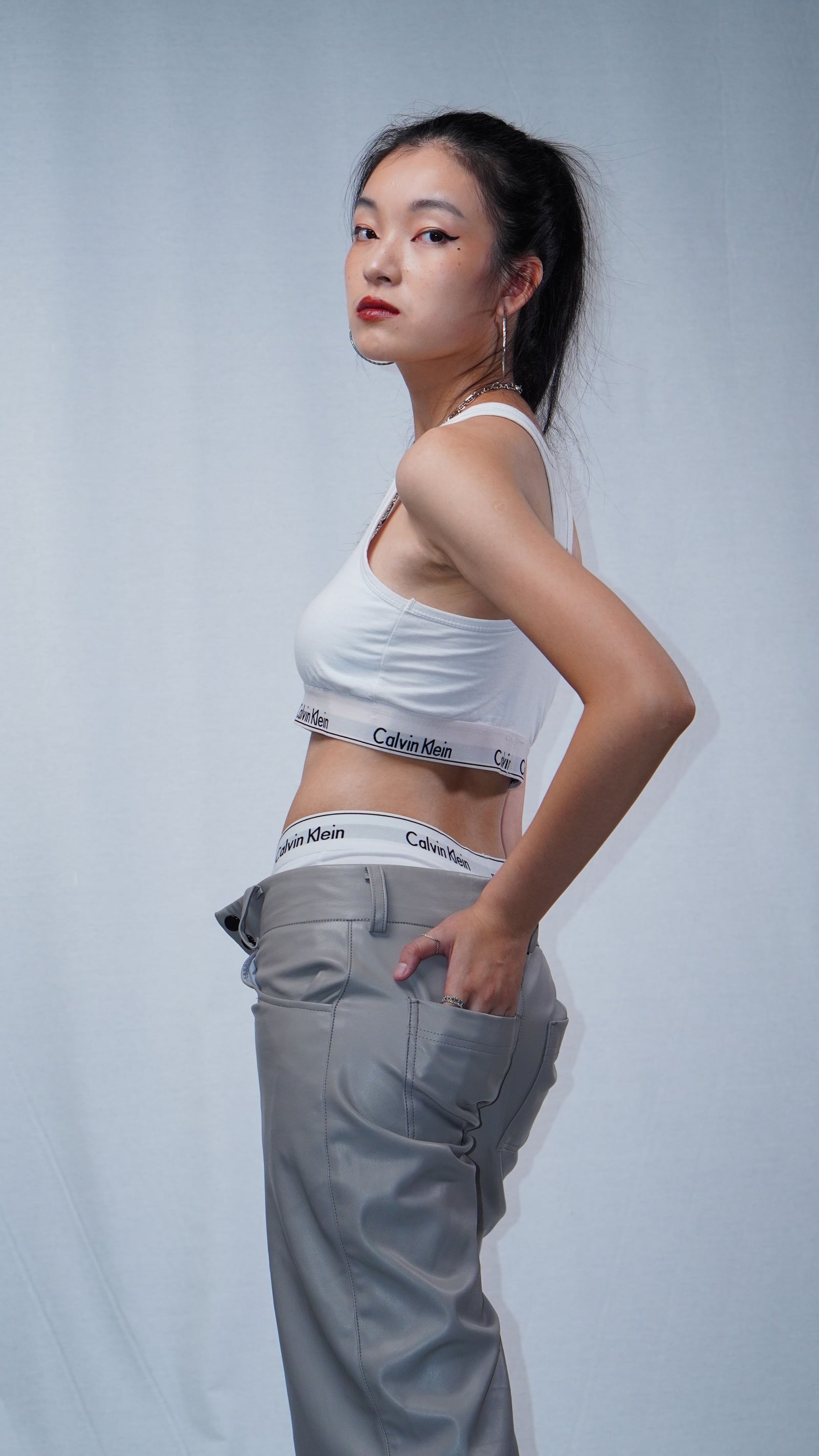A woman in a white top and gray trousers against a light studio background