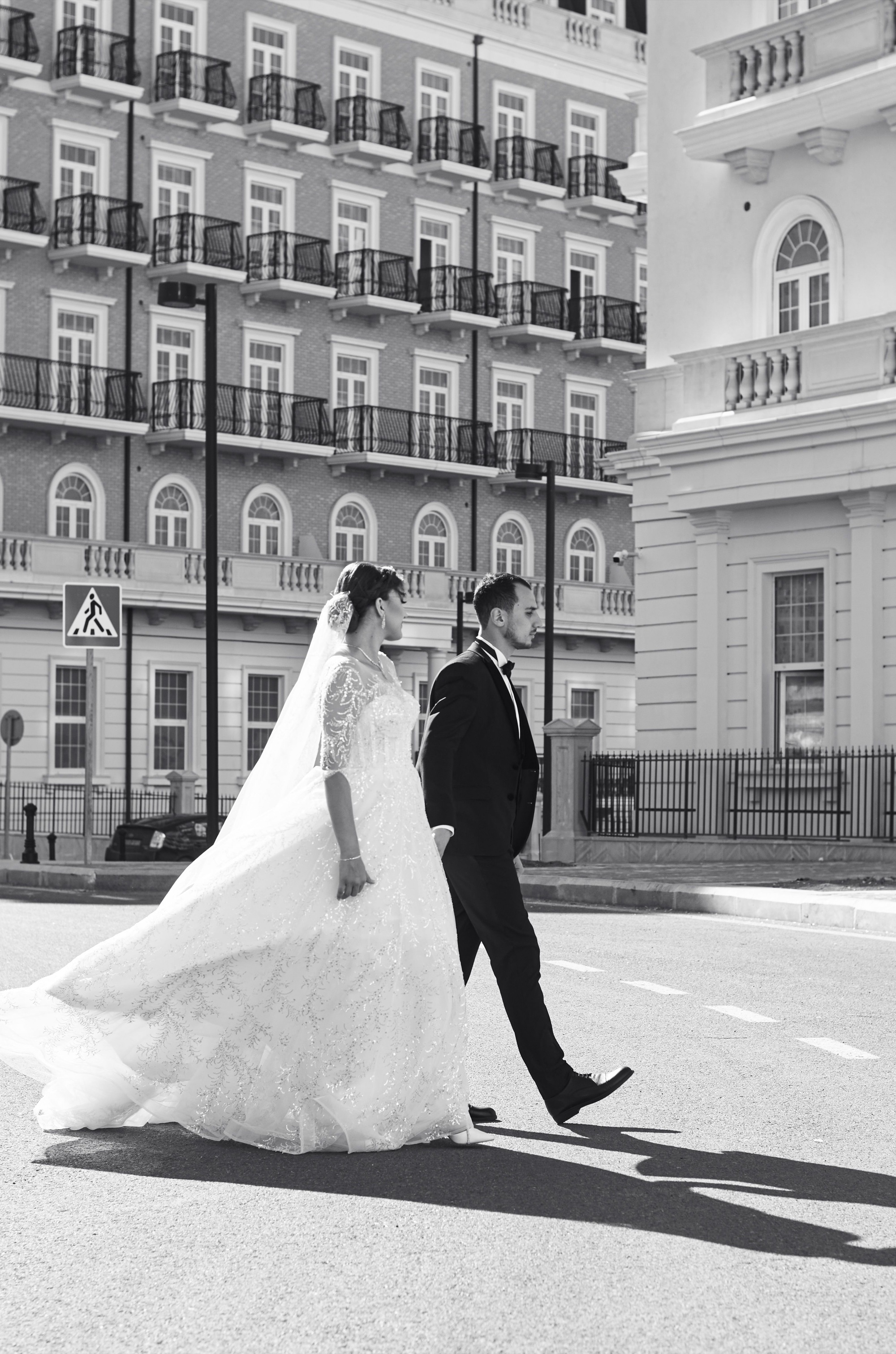 A bride and groom walking through a city square, with a flowing wedding train