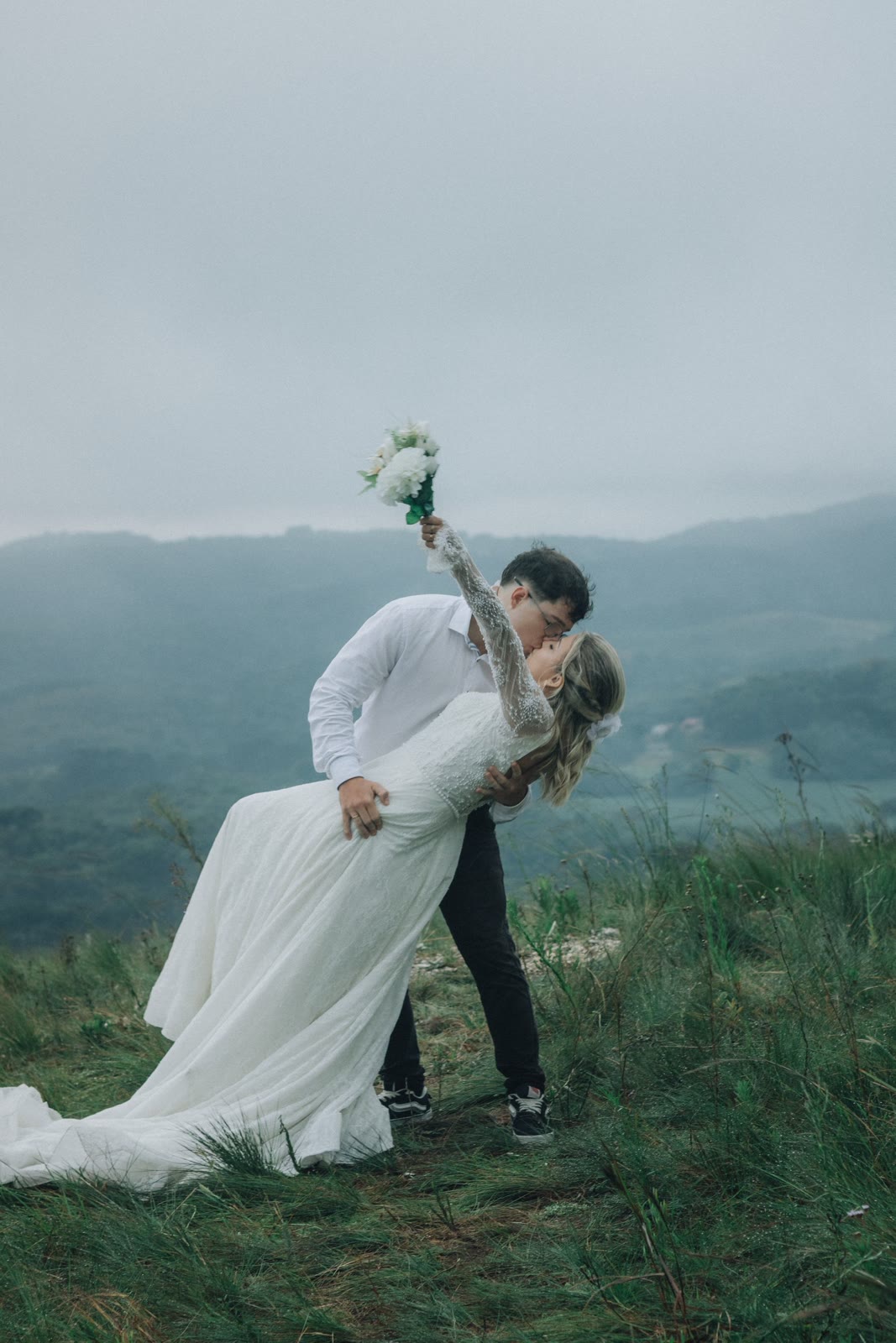 A newlywed couple embracing against a quiet mountain landscape.