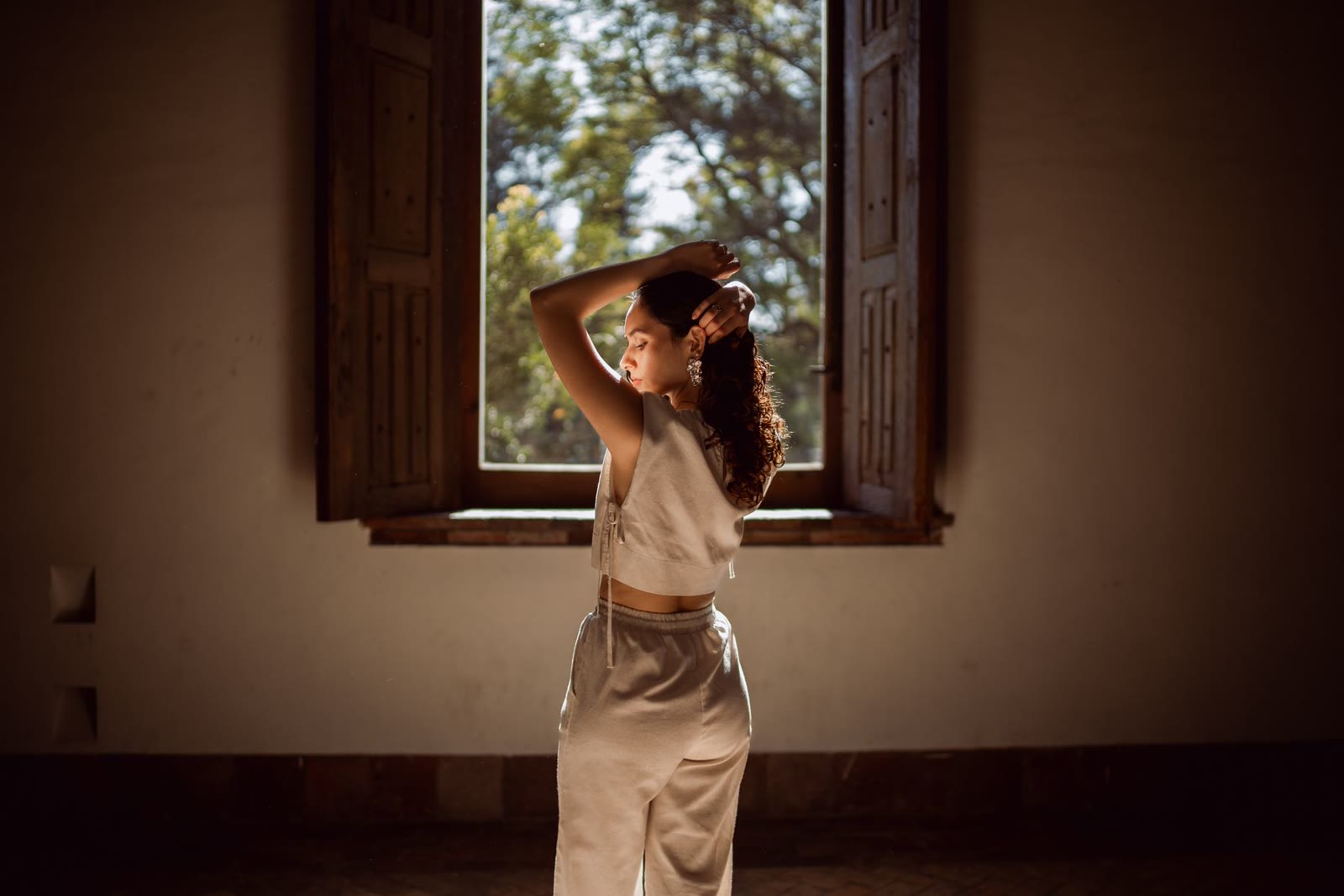 A woman in warm window light against a rustic interior.